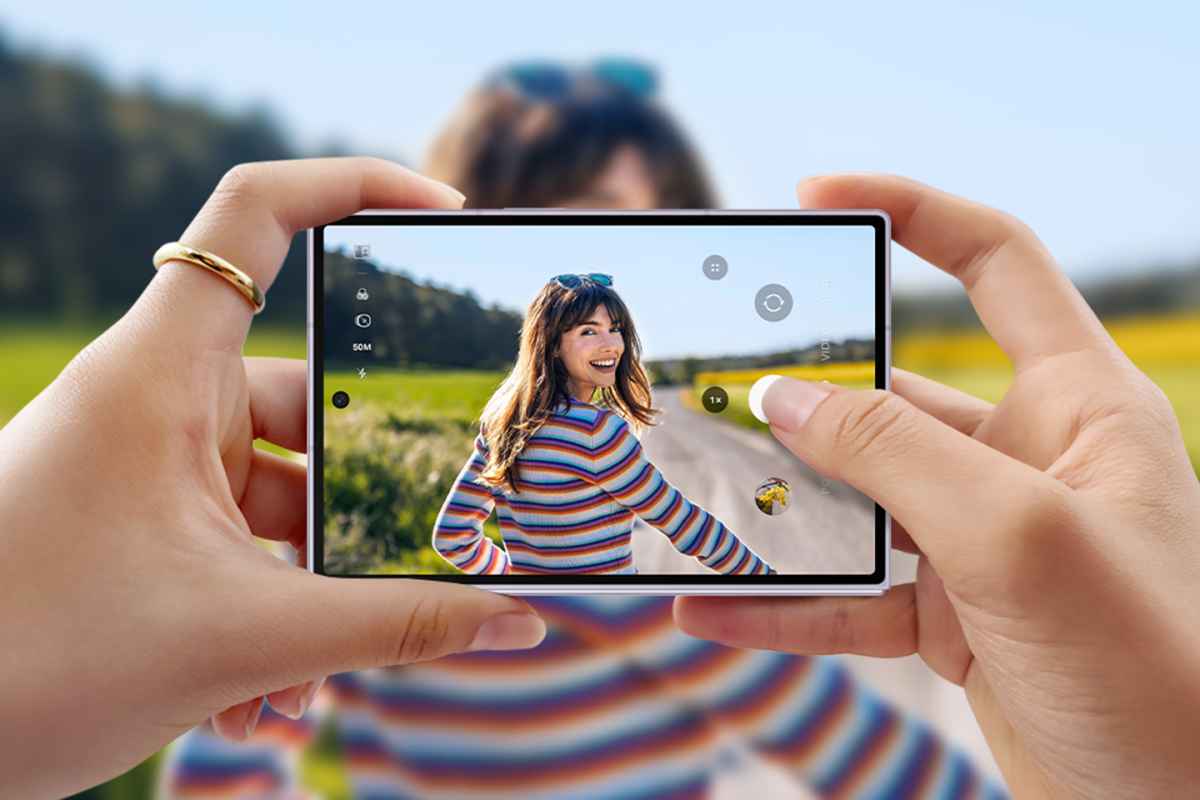 Rankos laiko telefoną, kuriuo fotografuojama moteris spalvotu dryžuotu megztiniu lauke.